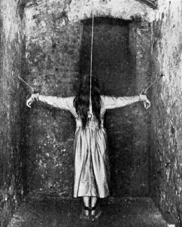 A woman stands in a narrow cell with her arms strapped to the wall,circa 1890. She is undergoing treatment for mental illness in 19th century Germany.